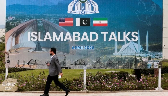 A man walks past a billboard near the media centre as delegations from the United States and Iran are expected to hold peace talks in Islamabad, on April 11, 2026. — Reuters