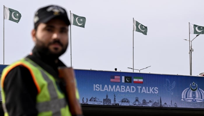 A policeman stands guard in front of a digital screen displaying news of US–Iran peace talks along a road in Pakistans capital Islamabad. — AFP