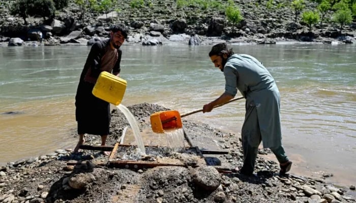 This photograph taken on April 13, 2026 shows Afghan men pouring water over a seive as they sift through mountainside stones in search of gold nuggets along the Kunar river in the Song area of Ghaziabad district, Kunar province. — AFP