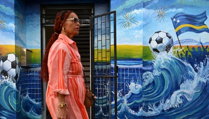 A woman walks past a mural depicting a football and the flag of Curacao in Willemstad, capital of the Dutch Caribbean island which is gripped by World Cup fever. —AFP