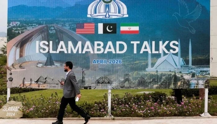 A man walks past a billboard near the media centre as delegations from the United States and Iran are expected to hold peace talks in Islamabad, on April 11, 2026. — Reuters