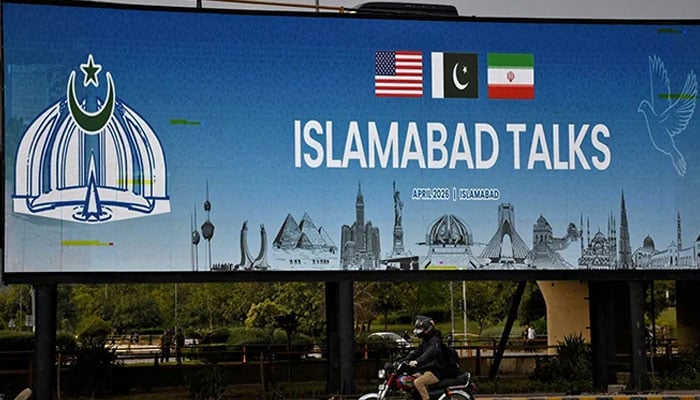 A man rides his motorbike past a billboard installed alongside a road as Pakistan prepares to host the US and Iran for peace talks, Islamabad, April 10, 2026. — Reuters