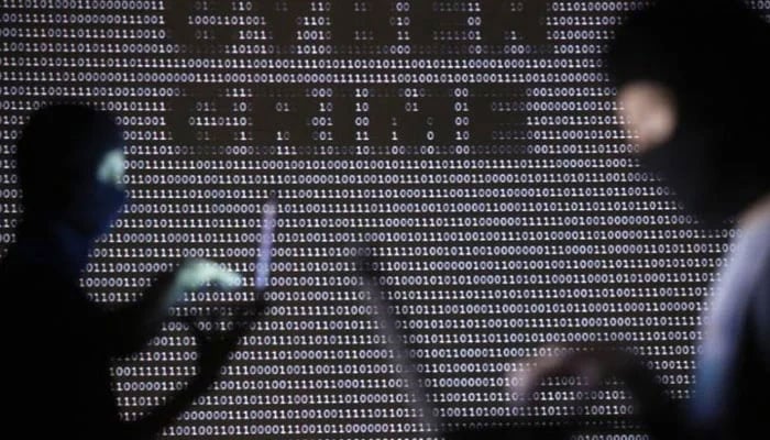 Representational image of people wearing balaclavas are silhouetted as they pose with a laptops in front of a screen projected with the word cyber crime and binary code, in this picture illustration. — Reuters/File