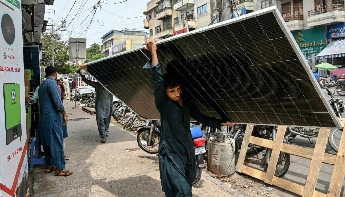 In this photograph taken on June 23, 2025, a labourer carries a solar panel along a road in Karachi. — AFP