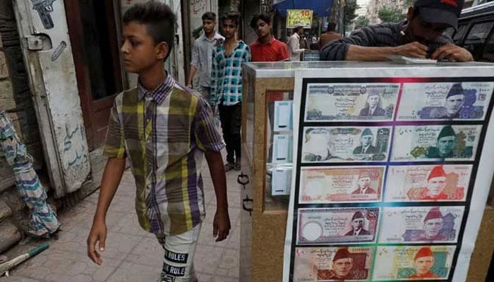 A boy walks past a sidewalk money exchange stall decorated with pictures of banknotes in Karachi on September 30, 2021. — Reuters