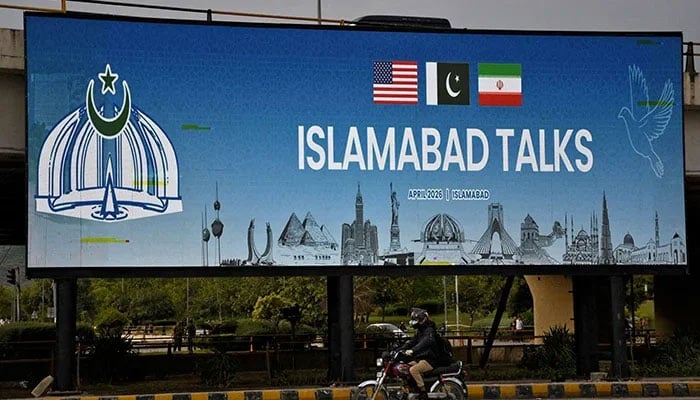 A man rides his motorbike past a billboard installed alongside a road as Pakistan prepares to host the US and Iran for peace talks, Islamabad, April 10, 2026. — Reuters