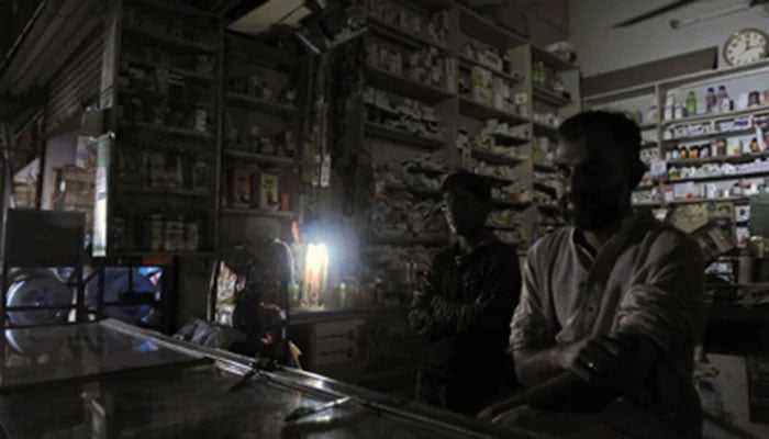 The representational image shows shopkeepers sitting inside their shop during a power outage. — The News/File