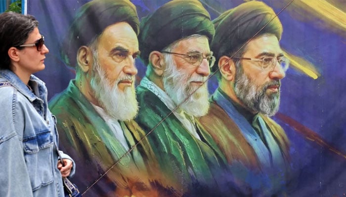 A woman walks past a banner featuring Iran´s late supreme leaders Ayatollah Ruhollah Khomeini (left) and Ayatollah Ali Khamenei (centre) next to newly elected supreme leader Ayatollah Mojtaba Khamenei, in Tehran on April 19, 2026. — AFP