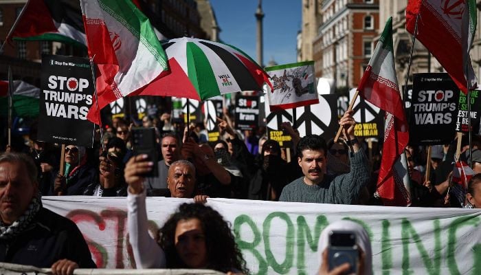 Protesters carry placards and wave Iranian flags on Whitehall during of a protest march in central London on March 21, 2026, against US-Israel war on Iran. — AFP