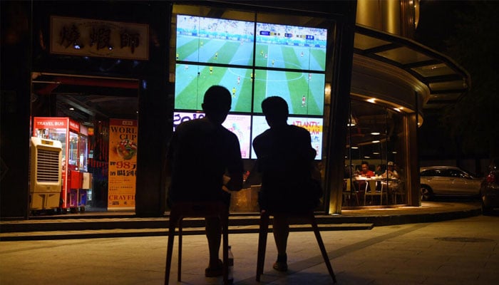Two persons watching a football match on a big screen. —AFP/File