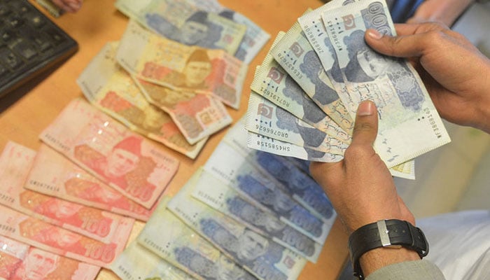 A money changer counts Pakistans currency at a market in Karachi on January 6, 2023. — AFP