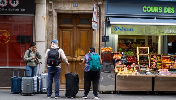 Tourists with suitcases in front of an apartment looking for their Airbnb in Paris, June 2, 2024. — AFP