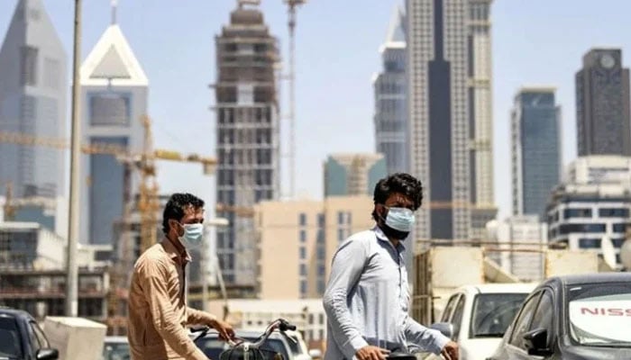 Foreign workers clad in mask walk pushing bicycles along a street in the Satwa district of Dubai on May 6, 2020. — AFP