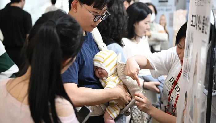 This picture taken on April 30, 2026 shows a man testing a baby carrier using a baby doll at a booth during a baby fair in Seoul. — AFP