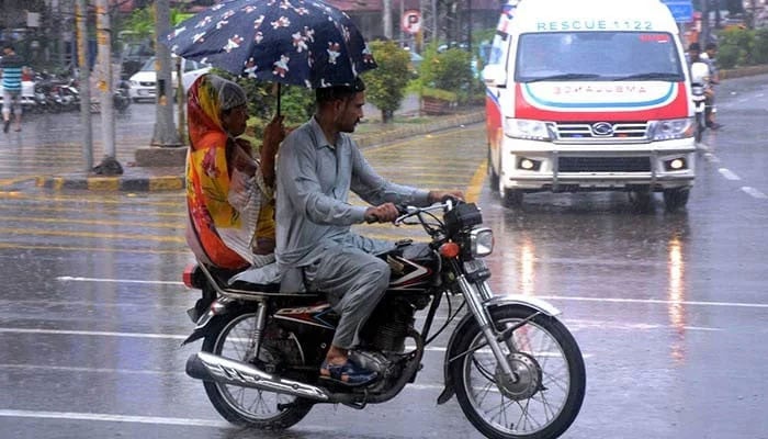 A woman holds an umbrella to shield her family from the rain while riding a motorcycle in Lahore on July 6, 2024. — AFP