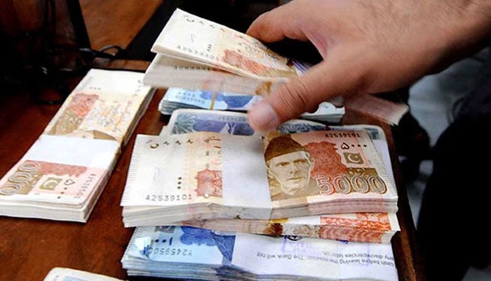 A person can be seen arranging stacks of PKR notes. — AFP/File