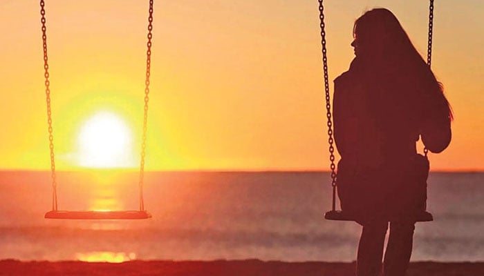 The image features a silhouette of a woman sitting alone on a beach swing at sunset. — Facebook@ColegioProfesionalesPsicologiaCR/File