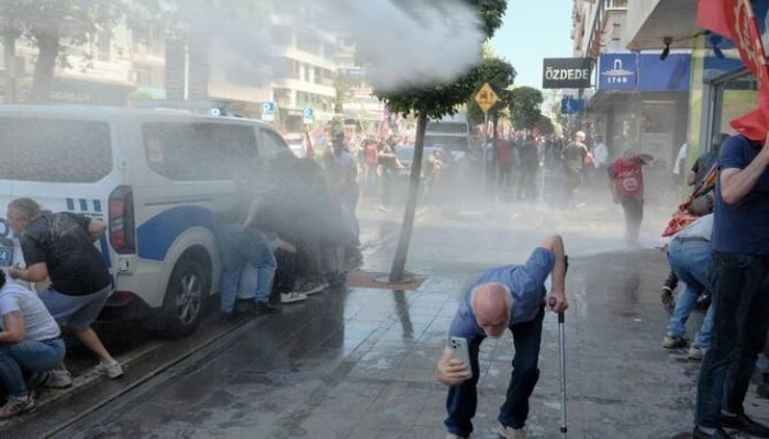 People take cover as Turkish riot police use water cannon to disperse protesters during a rally called by ousted opposition leader Ozgur Ozel, days after a court dismissed him from office, in Izmir on May 26, 2026. —AFP