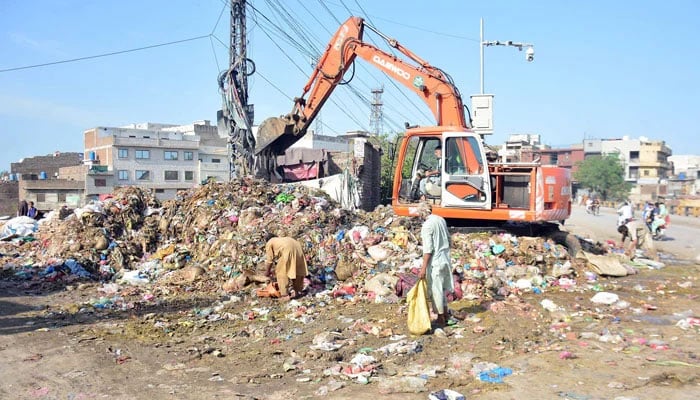 Workers cleaning sacrificial animal remains with the help of heavy machinery alongside a road in Rawalpindi on June 19, 2024. — Online