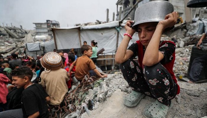 A girl puts a pot to her head as Palestinians wait to receive food cooked by a charity kitchen, in Beit Lahia, northern Gaza Strip, April 24, 2025. — Reuters