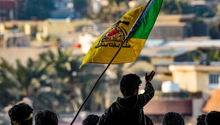 People waving the flag of the group Kataeb Hezbollah. —AFP/File