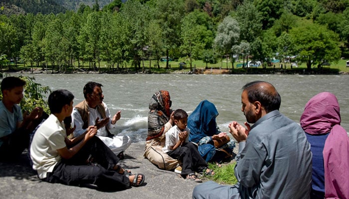 This photograph, taken on May 29, 2026, shows family members of Raja Liaqat, sitting along the banks of the Neelum River and offering prayers for his soul along with relatives across the Line of Control in Indian-administered Kashmir, as seen from Keran village in Pakistan-administered Kashmir. — AFP