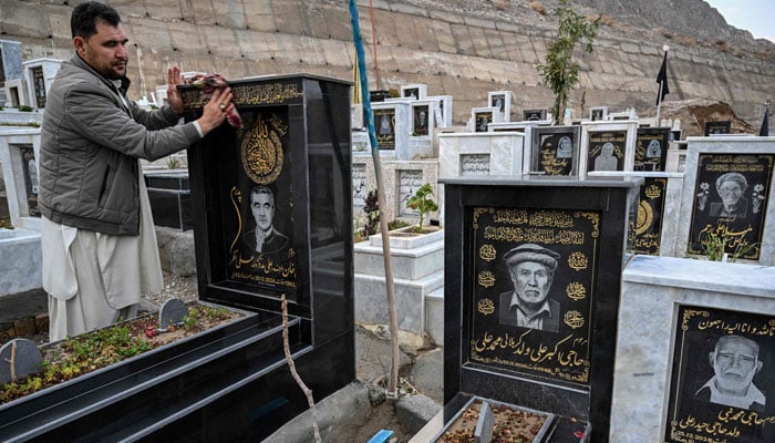 This photograph, taken on February 17, 2026, shows a resident, Talib Hussain, cleaning the tombstone with an engraved portrait of his deceased father at a graveyard in Quetta. — AFP