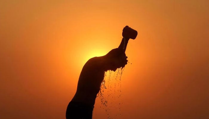 A labourer is silhouetted against the setting sun as he bathes on a hot summer day on Jun 1, 2024. — AFP