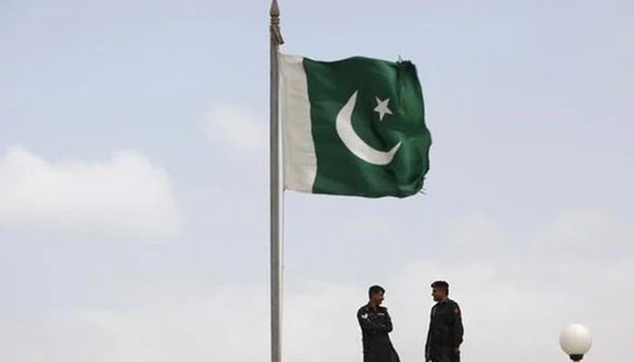 A Pakistani flag flies on a mast as paramilitary Frontier Corps soldiers talk while guarding at Karachis District Malir prison, August 23, 2013. — Reuters