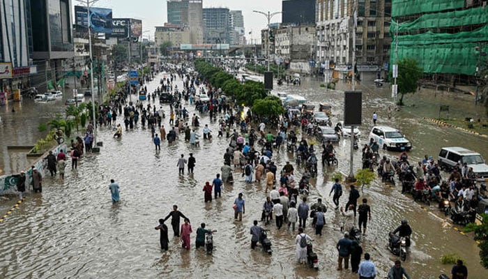 People wade through a flooded street after heavy rainfall in Karachi on August 19, 2025. — AFP