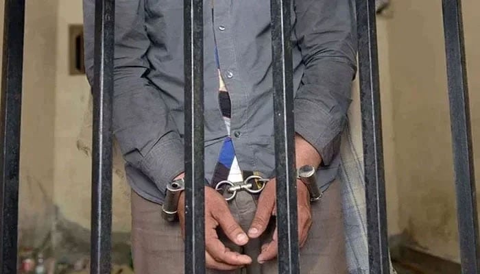 A representational image showing a person handcuffed and standing behind bars. — AFP/File