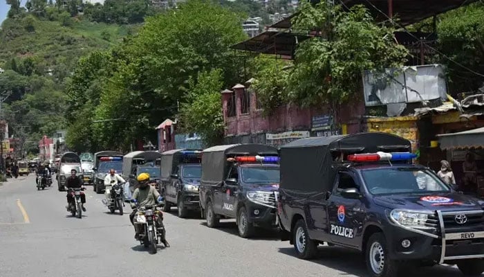 Commuters ride past security personnel as they patrol a street ahead of a protest by the Joint Awami Action Committee (JAAC) in Muzaffarabad, on June 7, 2026. — AFP