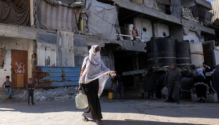 A woman walks with a water container after topping up from a cistern at a shelter camp for people displaced by war, in Khan Yunis in the southern Gaza Strip on June 6, 2026. —AFP