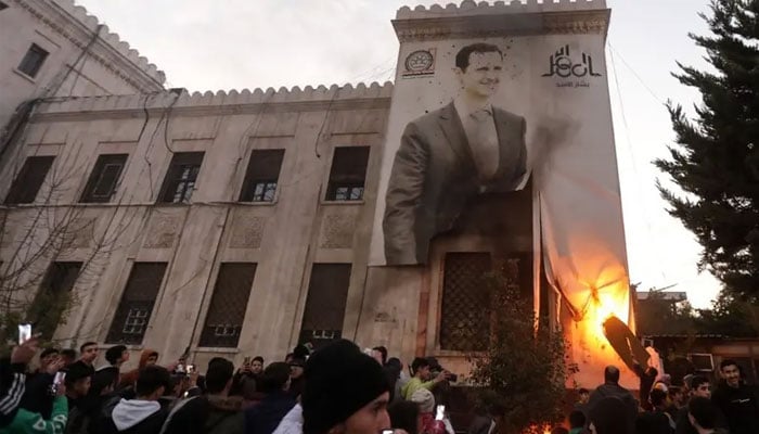 Residents in Hama set ablaze a large banner bearing a picture of Syria’s President Bashar al-Assad hanging on the facade of a municipal building on December 5, 2024, after armed opposition factions took control of Syria’s west-central city. —AFP