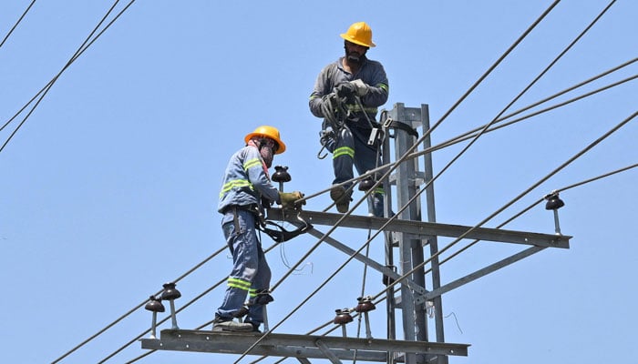 Electricians work on high-voltage power lines in Lahore on June 14, 2026. — AFP