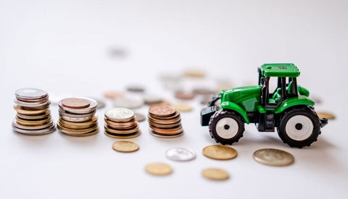 A mini green tractor beside stacks of coins in this representational image. — Pexels/File