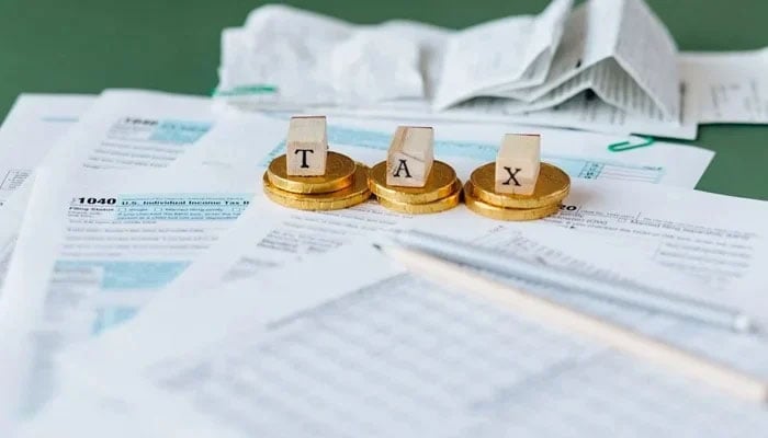 A representational image of a table where coins and cubes with tax letters written on them are placed on the papers. — Pexels/File