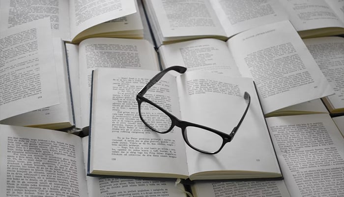 Representational image shows a pair of black-rimmed reading glasses resting folded on top of an open book. — Unsplash