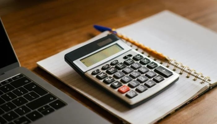 This representational image shows a calculator resting on a notebook next to a laptop. — Pexels/File