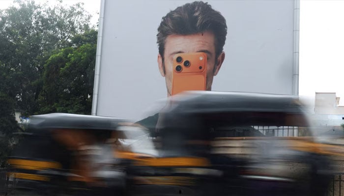 Auto rickshaws move past an Apple iPhone hoarding on a street in Mumbai, India, June 29, 2026.—Reuters