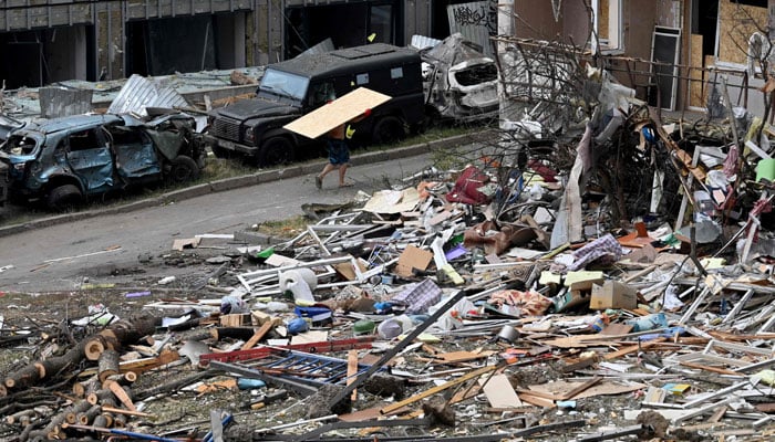 A local resident carries a plywood board past debris and a residential building damaged following a Russian air attack on the Ukrainian capital of Kyiv on July 3, 2026. — AFP
