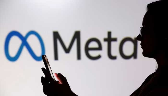A teenager poses for a photo while holding a smartphone in front of a Meta logo in this illustration taken September 11, 2025.