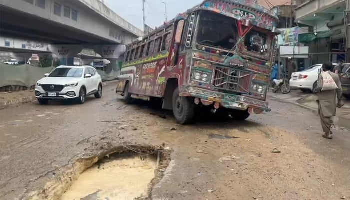 A passenger bus is stuck in a sinkhole created on the road after heavy rainfall in Karachi on August 19, 2025. — Geo News