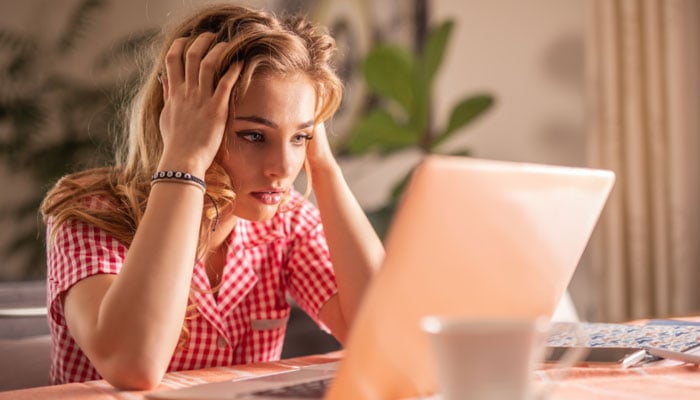 A representational image of a young woman looking anxious while working on her laptop. — Canva