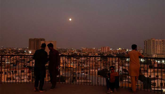 People pictured at a terrace while moon shines on the sky in Karachi on November 15, 2024. — Reuters
