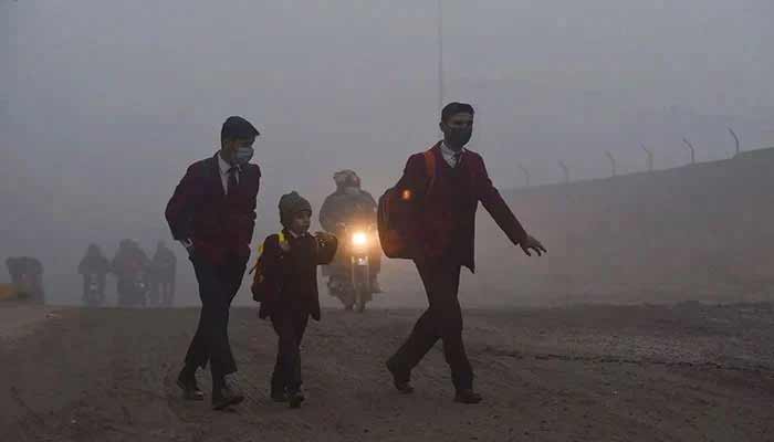 Children walk to their school along a street amid smoggy conditions early in the morning in Lahore. — AFP
