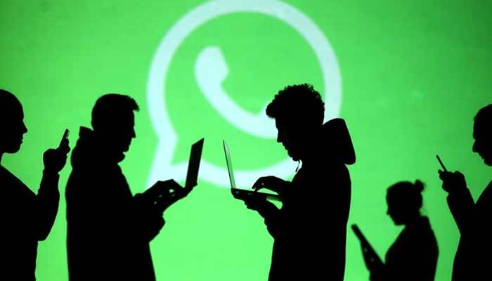 Silhouettes of laptop and mobile device users are seen next to a screen projection of Whatsapp logo in this picture illustration. — Reuters
