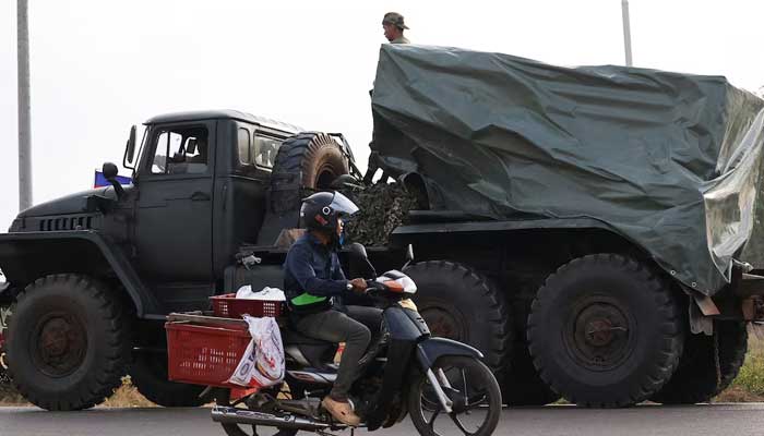 A man drives past a military vehicle heading towards the border, amid deadly clashes between Thailand and Cambodia along a disputed border area, in Srei Snam, Siem Reap Province, Cambodia on December 10, 2025. — Reuters