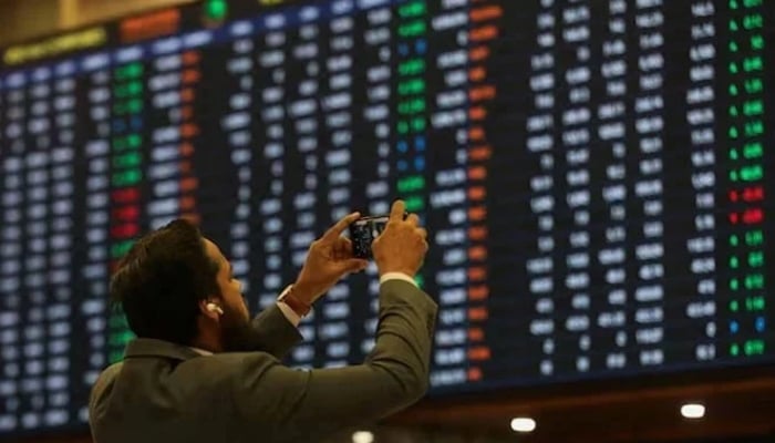 A man uses a mobile phone as he takes a photo of the electronic board displaying share prices during a trading session at the Pakistan Stock Exchange, Karachi. — Reuters/File