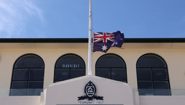 Australias flag flies at half-mast at the Bondi Surf Bathers Life Saving Club near the promenade of Bondi Beach, where mourners have left floral tributes to honour victims of the shooting that took place there on December 14, in Sydney on December 18, 2025. — AFP